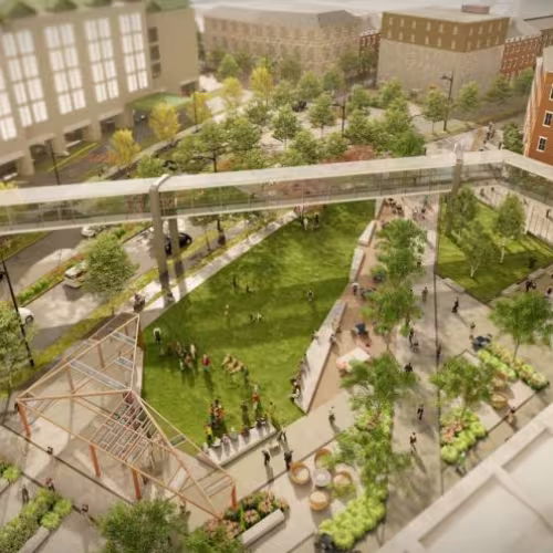 Digitally rendered bird&rsquo;s eye view of an irregular shaped park in a city centre, at dusk, with an angular pedway stretching overhead. The park is full of people, surrounded by a street with cars, and 5-story buildings. Angular pathways cut through the grassy park, with freestanding rectangular planters, green trees, and a wooden structure with a transparent roof and no walls.